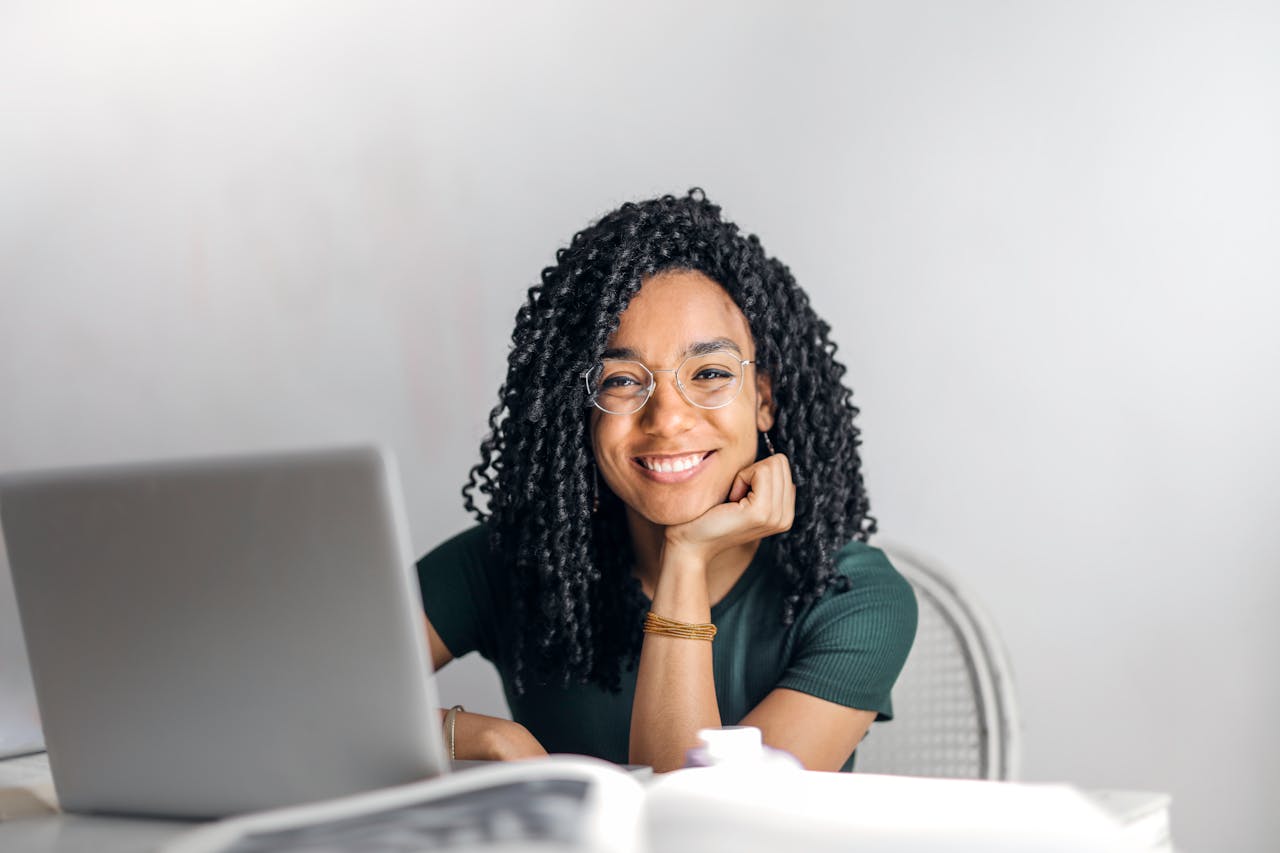 Mastering the First Impression: Your intriguing post title goes here Joyful businesswoman with curly hair smiling at camera while using laptop indoors.