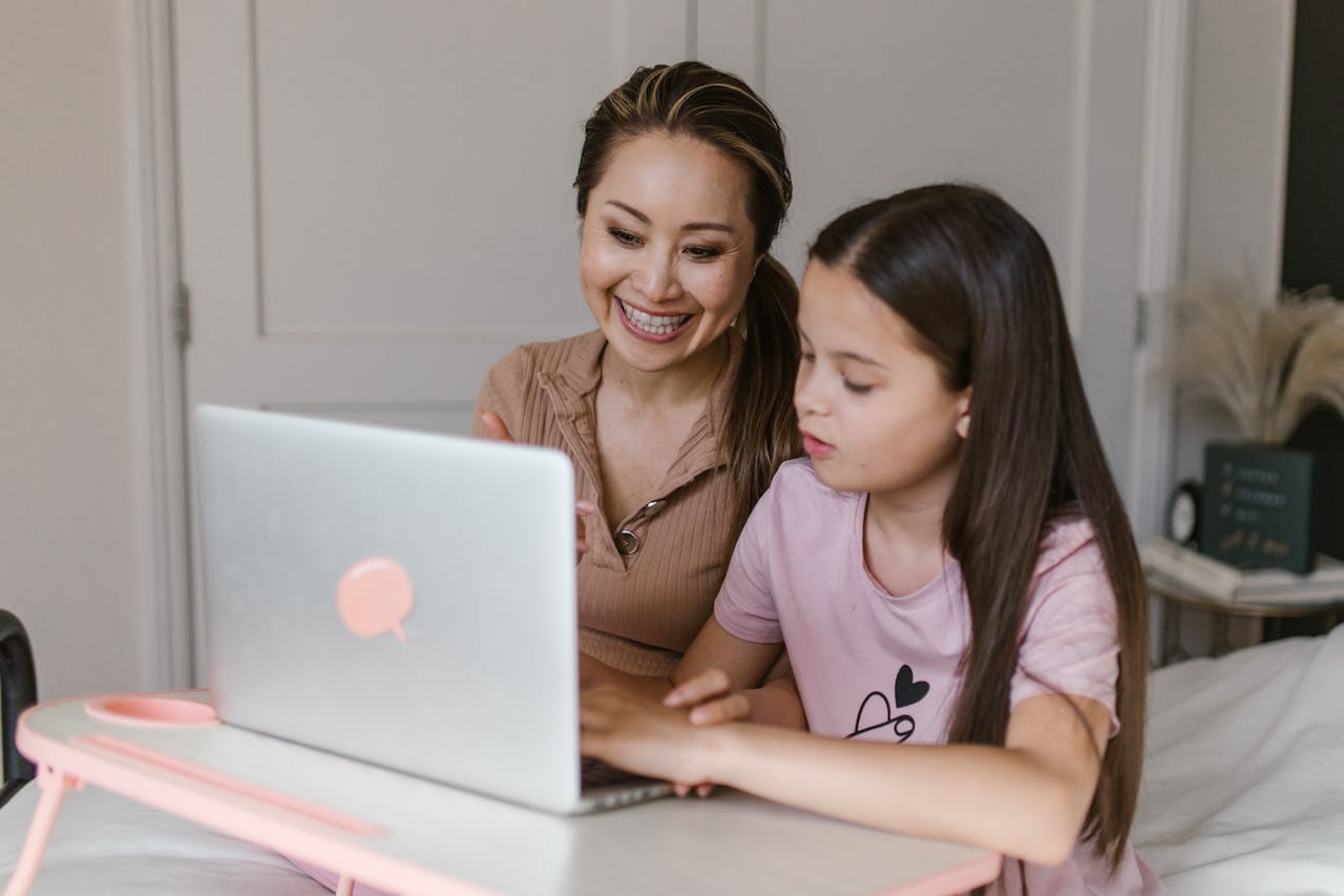 about-us A mother and daughter smile and learn together using a laptop at home.